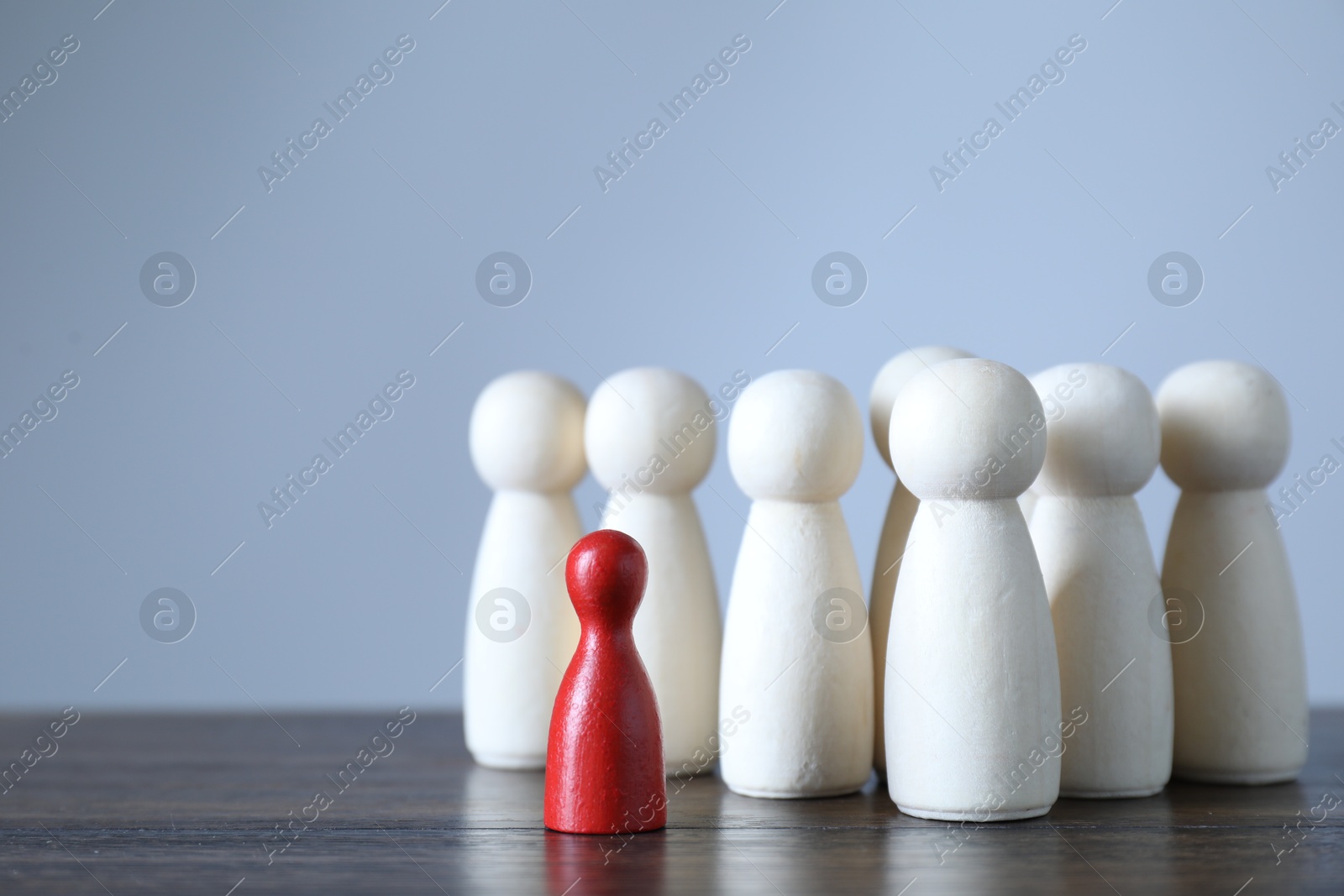 Photo of Human resources concept. Red figure among wooden ones on table against light background, closeup. Space for text