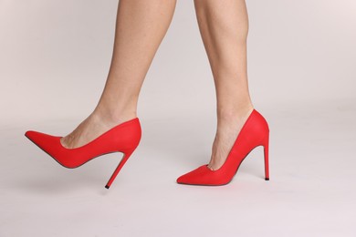 Photo of Woman wearing beautiful red high heeled shoes on white background, closeup