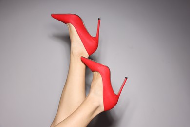 Photo of Woman wearing beautiful red high heeled shoes on light grey background, closeup