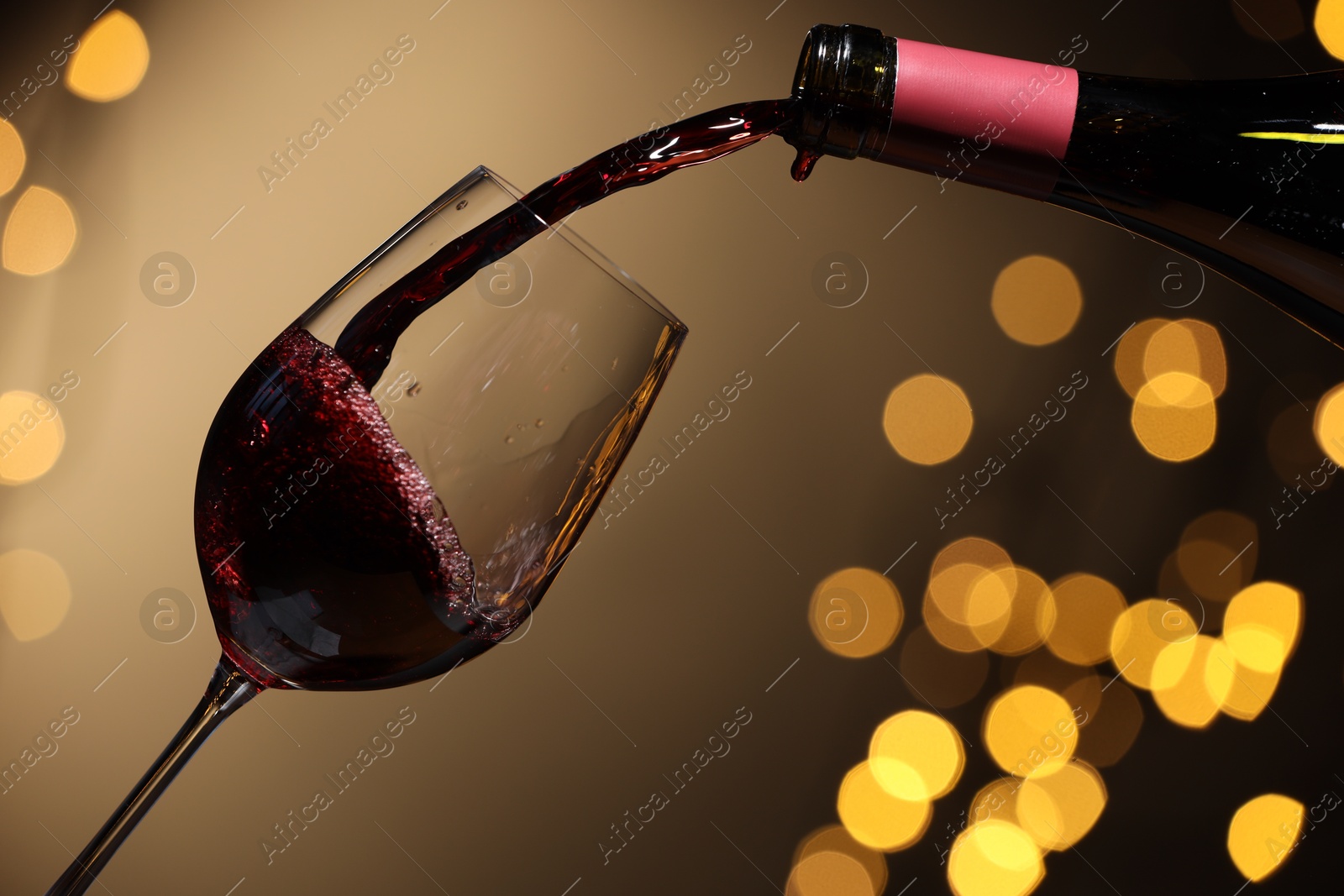 Photo of Pouring red wine into glass against beige background, closeup. Bokeh effect