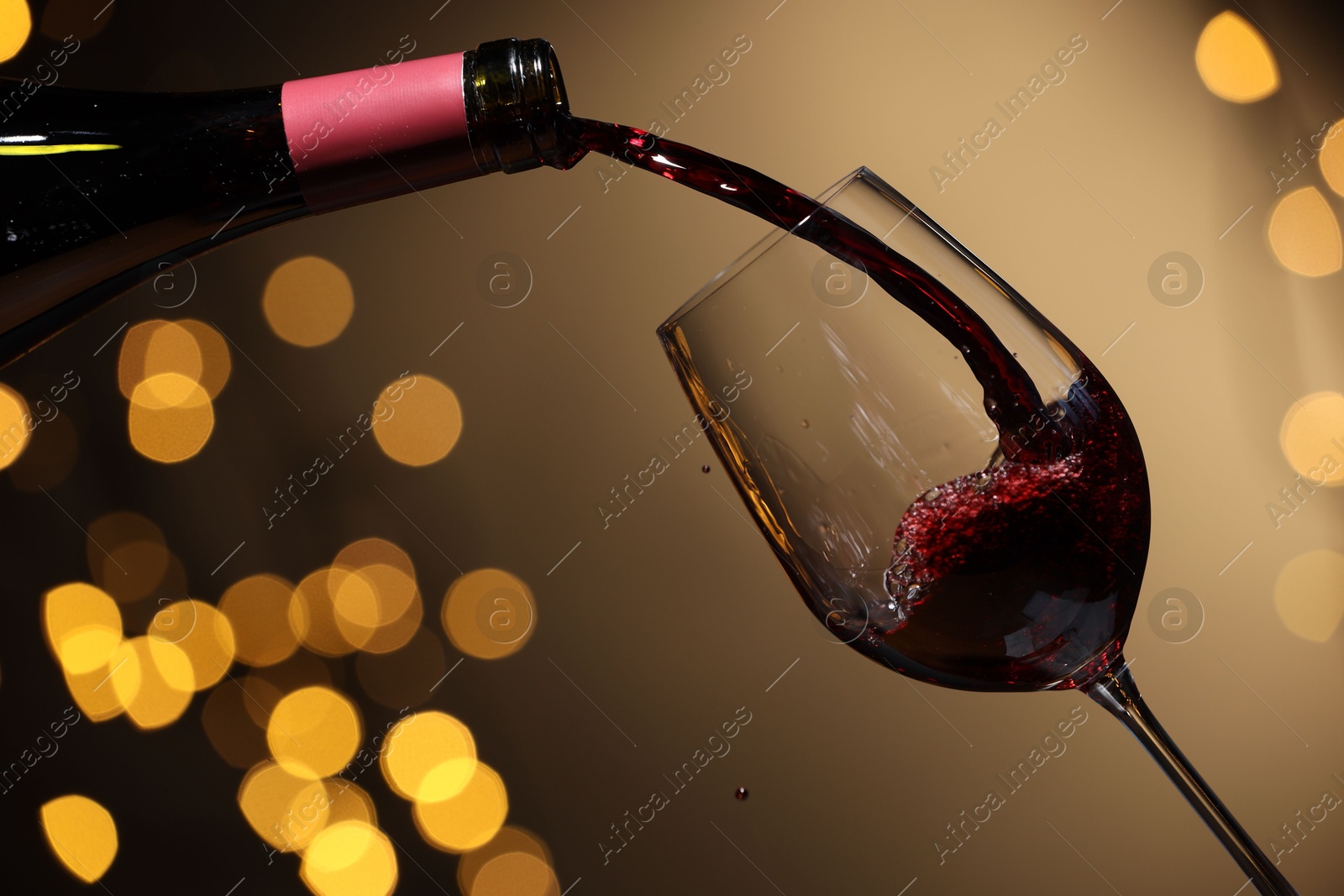 Photo of Pouring red wine into glass against beige background, closeup. Bokeh effect