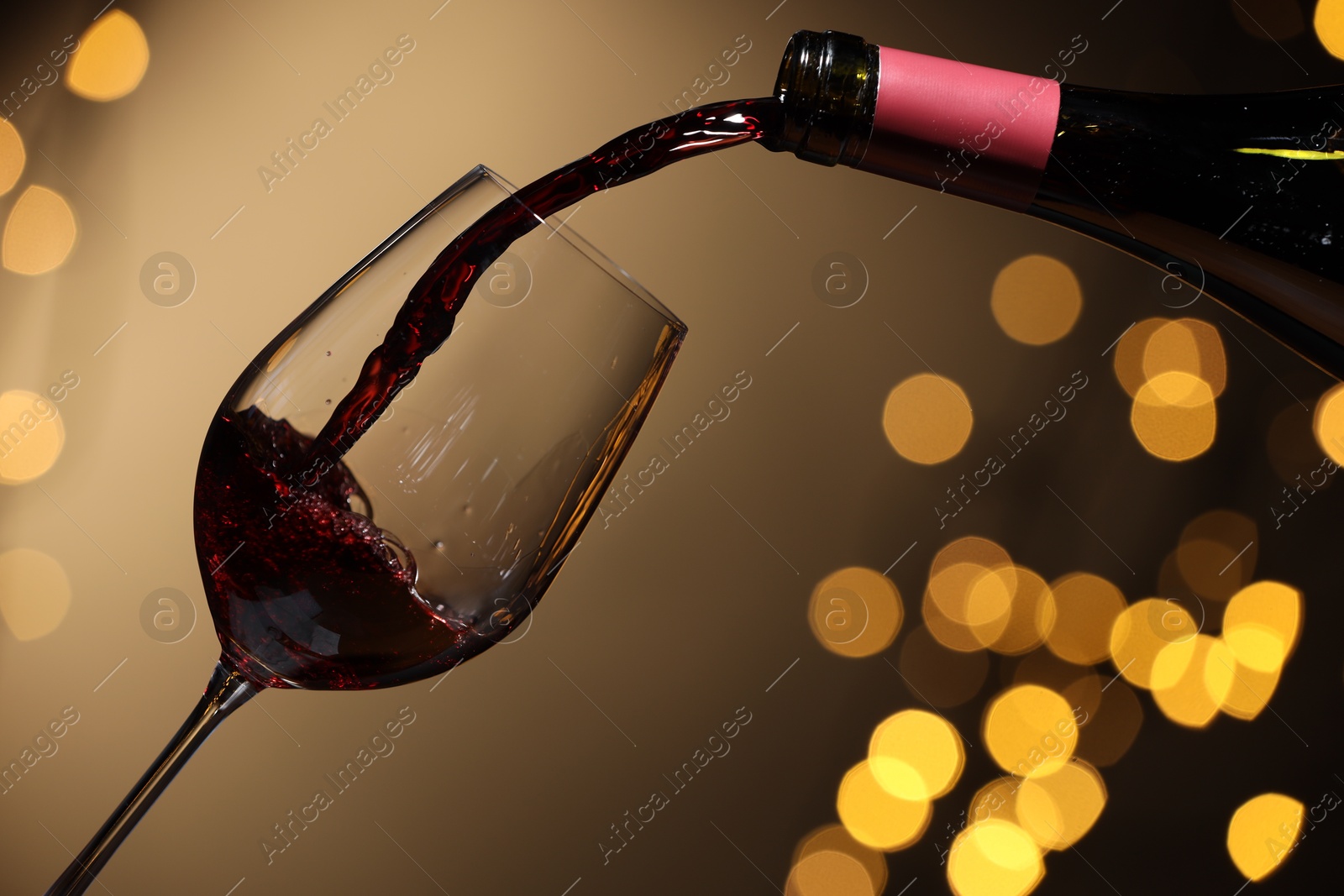 Photo of Pouring red wine into glass against beige background, closeup. Bokeh effect