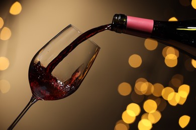 Photo of Pouring red wine into glass against beige background, closeup. Bokeh effect