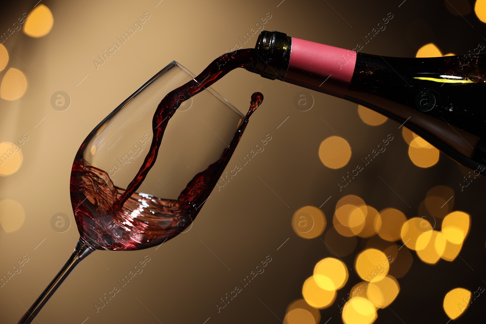 Photo of Pouring red wine into glass against beige background, closeup. Bokeh effect