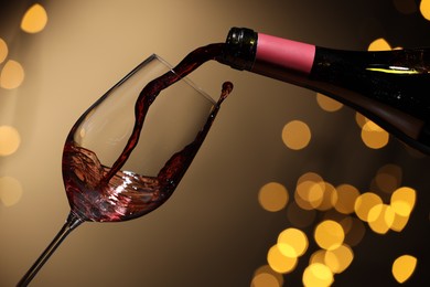 Photo of Pouring red wine into glass against beige background, closeup. Bokeh effect