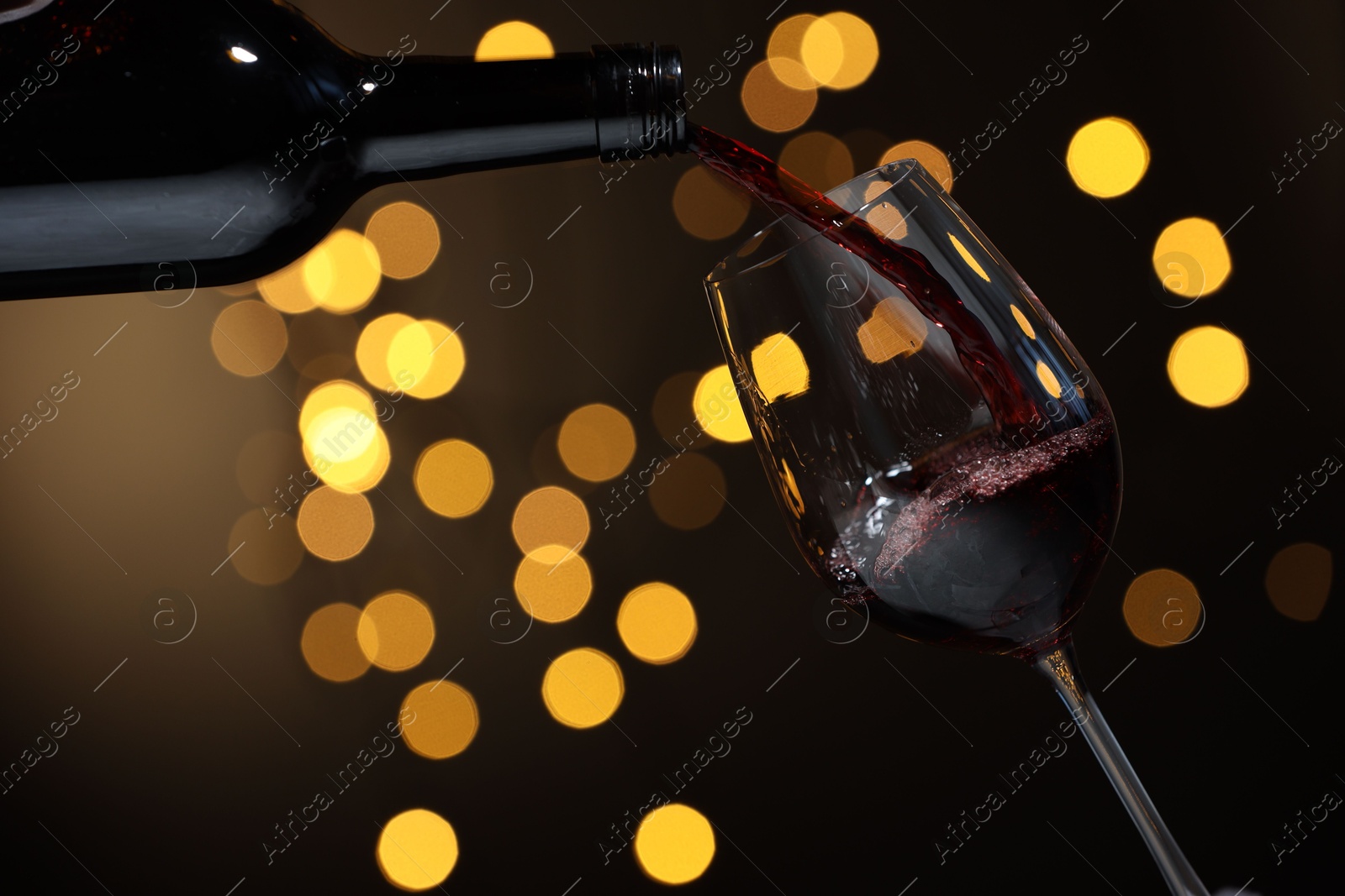 Photo of Pouring red wine into glass against beige background, closeup. Bokeh effect