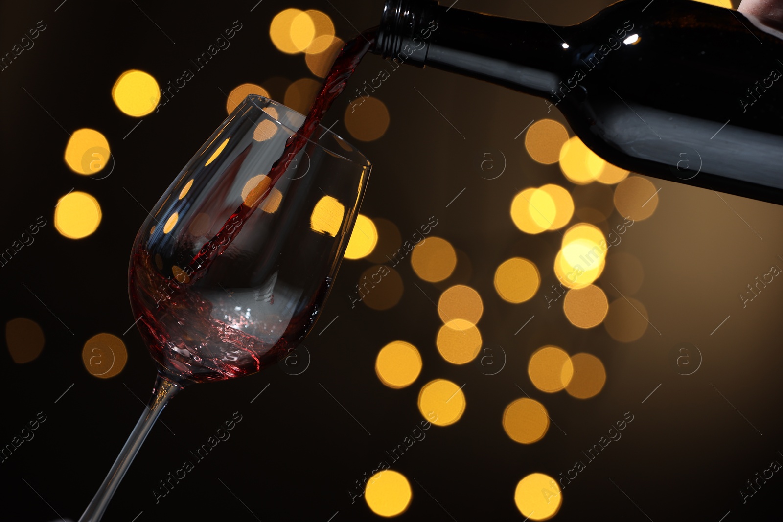 Photo of Pouring red wine into glass against beige background, closeup. Bokeh effect