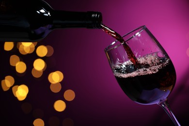 Photo of Pouring red wine into glass against purple background, closeup. Bokeh effect