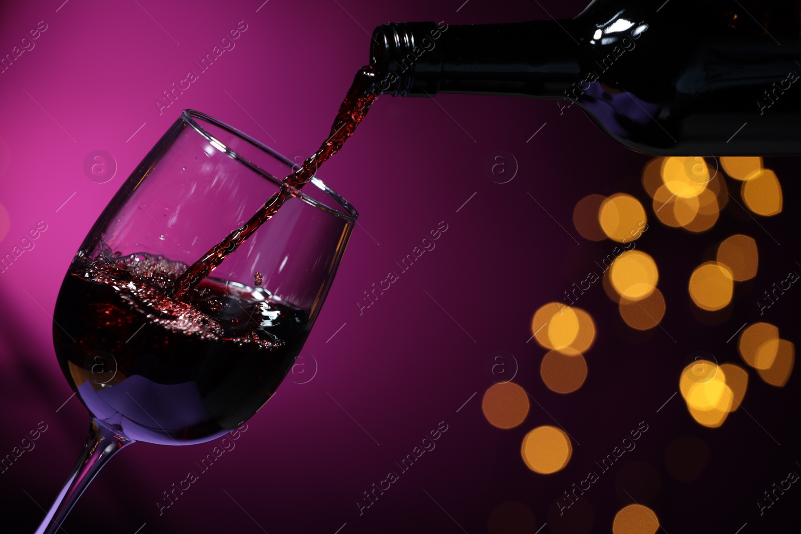 Photo of Pouring red wine into glass against purple background, closeup. Bokeh effect