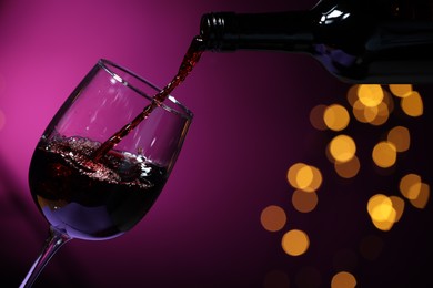 Photo of Pouring red wine into glass against purple background, closeup. Bokeh effect