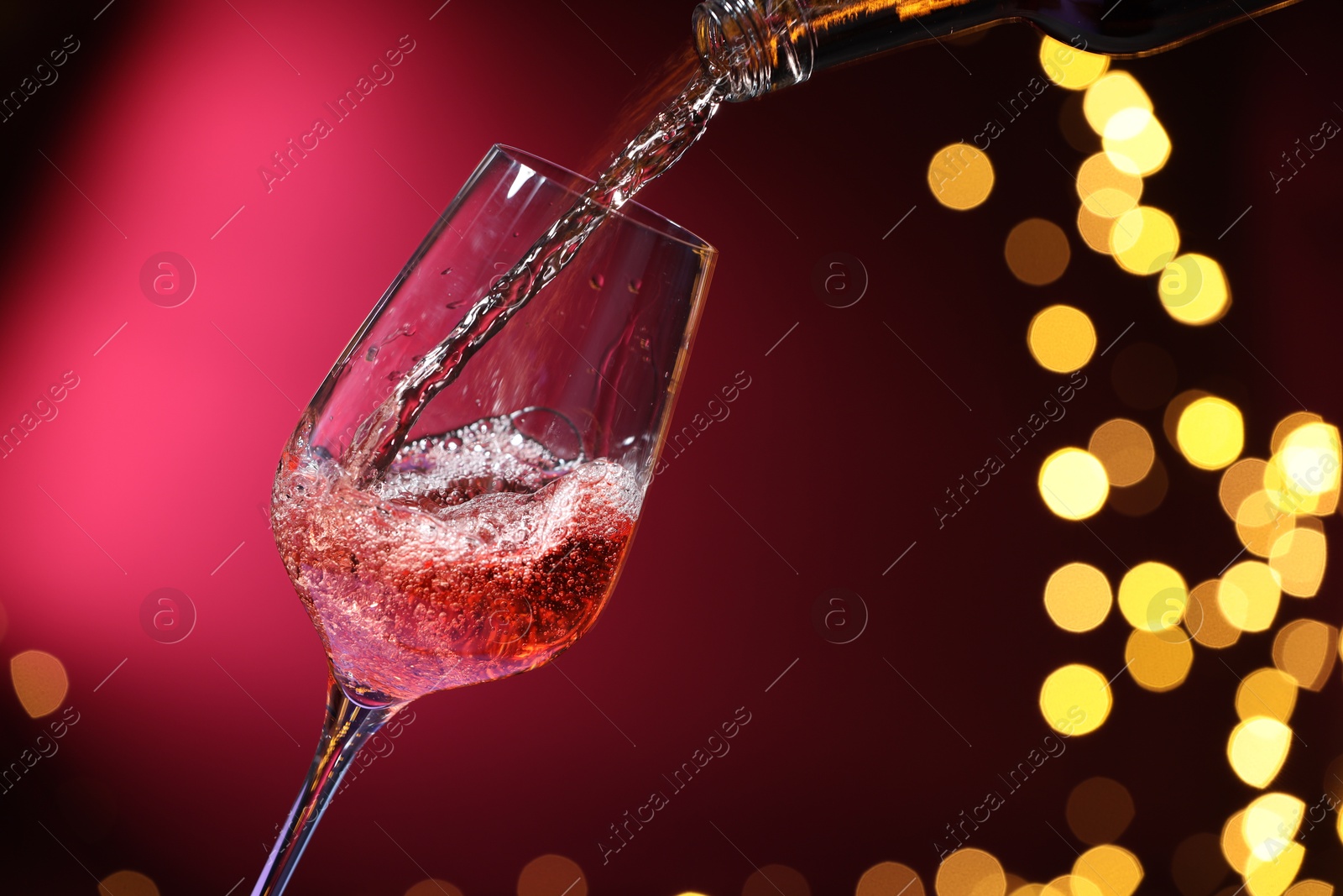 Photo of Pouring wine into glass against pink background, closeup. Bokeh effect