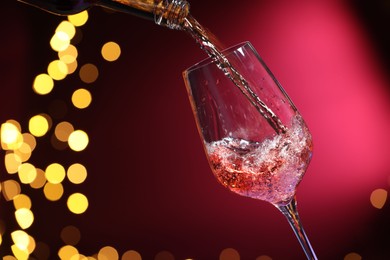 Photo of Pouring wine into glass against pink background, closeup. Bokeh effect