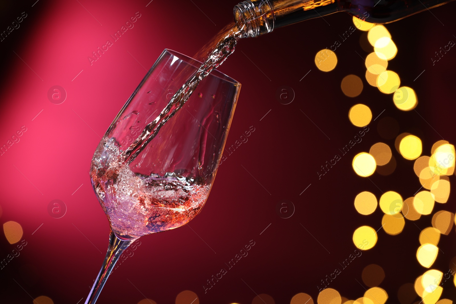 Photo of Pouring wine into glass against pink background, closeup. Bokeh effect