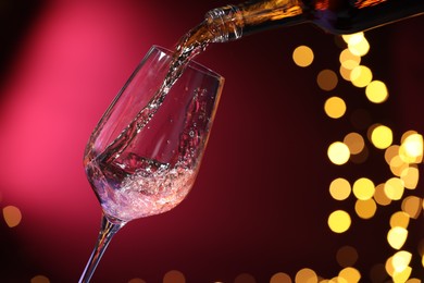 Photo of Pouring wine into glass against pink background, closeup. Bokeh effect