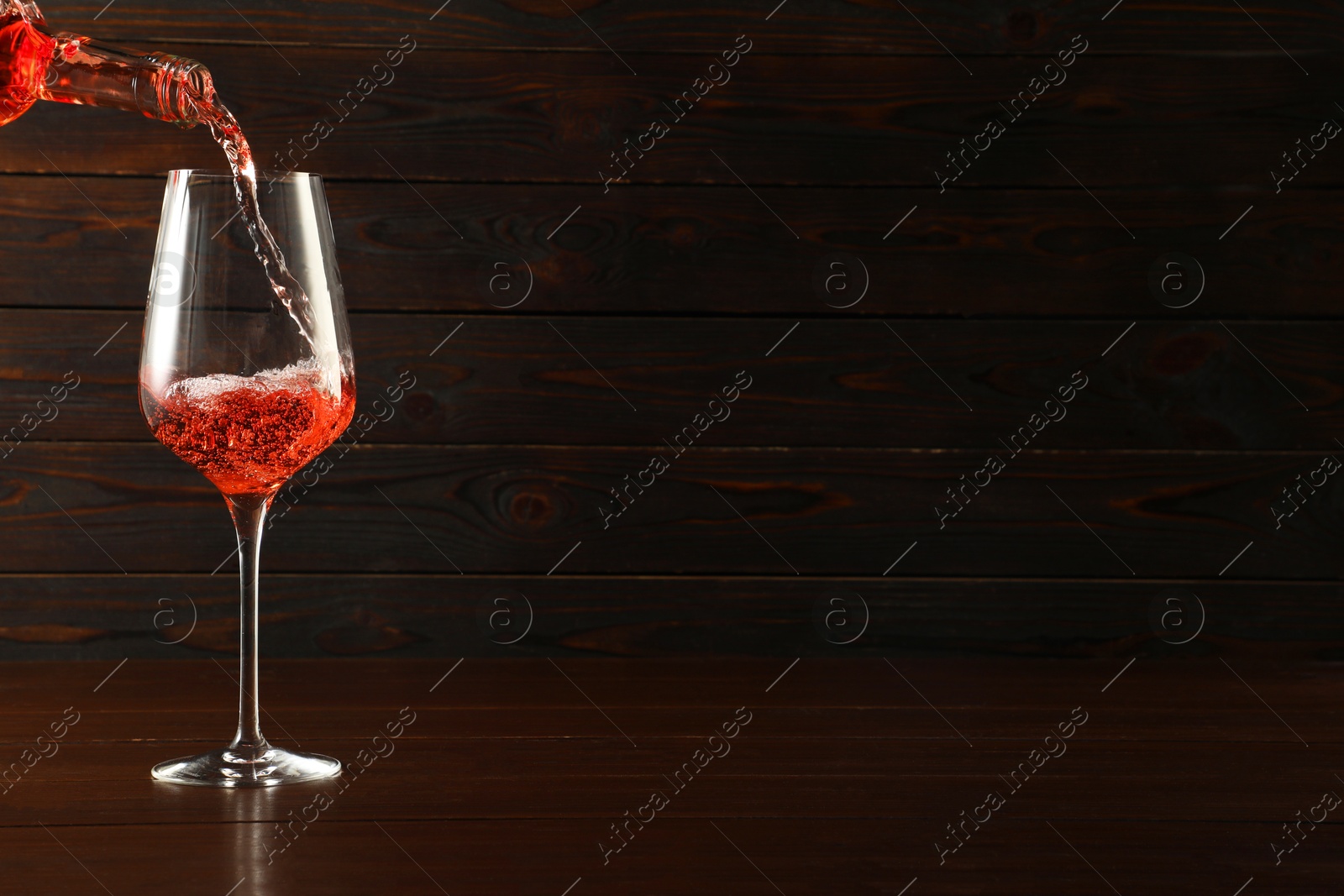 Photo of Pouring rose wine into glass at wooden table, space for text