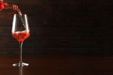 Photo of Pouring rose wine into glass at wooden table, space for text