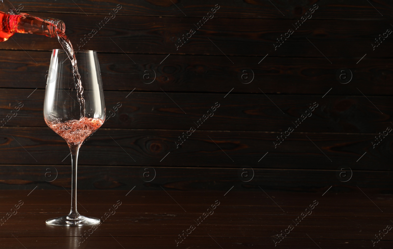 Photo of Pouring rose wine into glass at wooden table, space for text