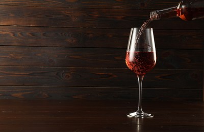 Photo of Pouring rose wine into glass at wooden table, space for text