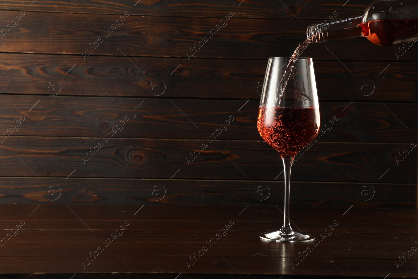 Photo of Pouring rose wine into glass at wooden table, space for text