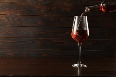 Photo of Pouring rose wine into glass at wooden table, space for text