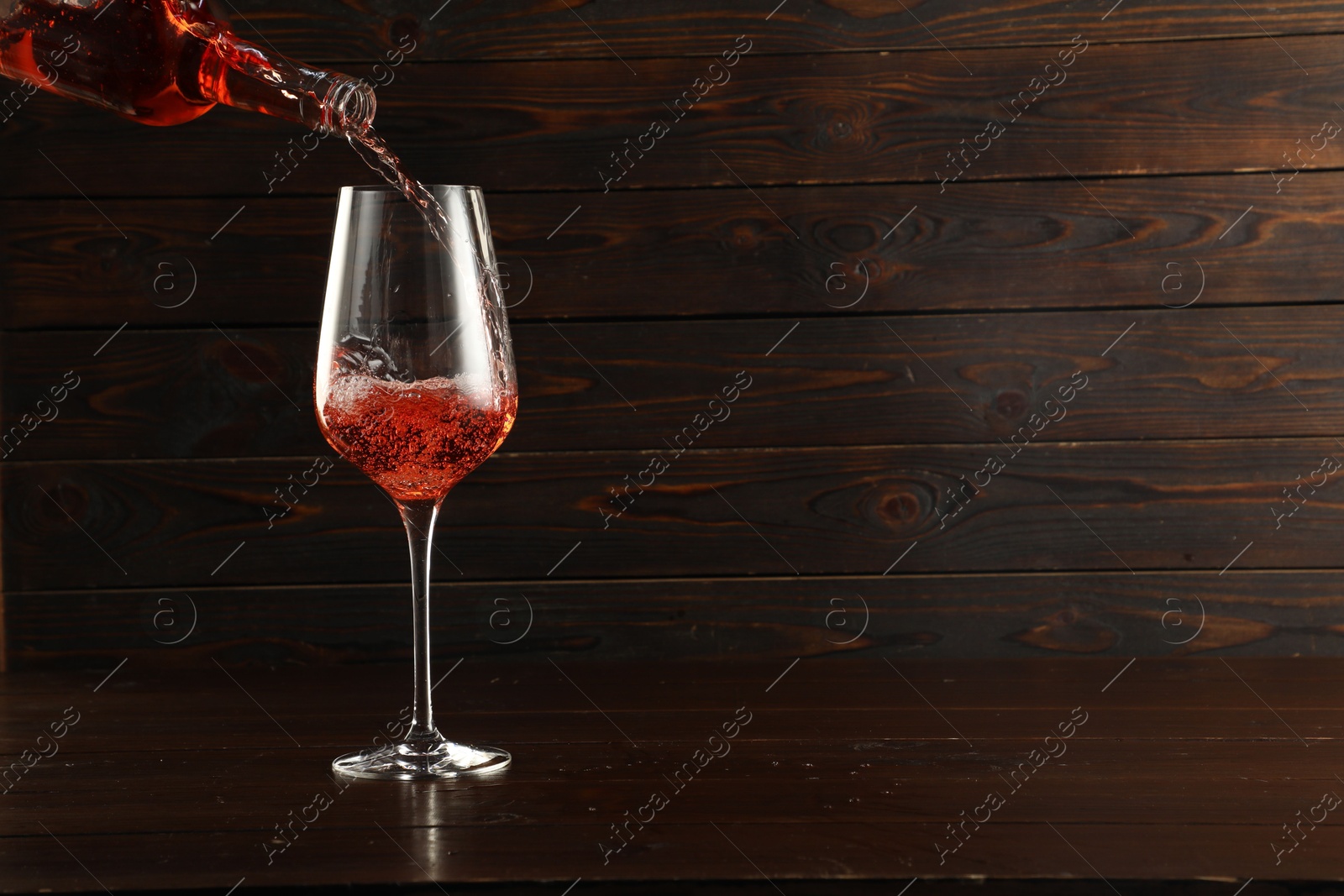 Photo of Pouring rose wine into glass at wooden table, space for text