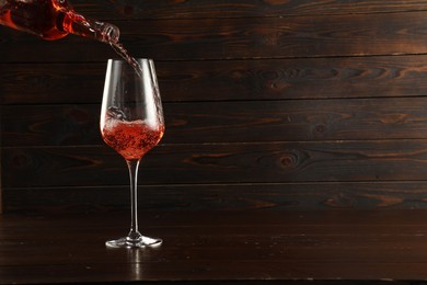 Photo of Pouring rose wine into glass at wooden table, space for text