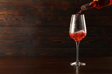 Photo of Pouring rose wine into glass at wooden table, space for text