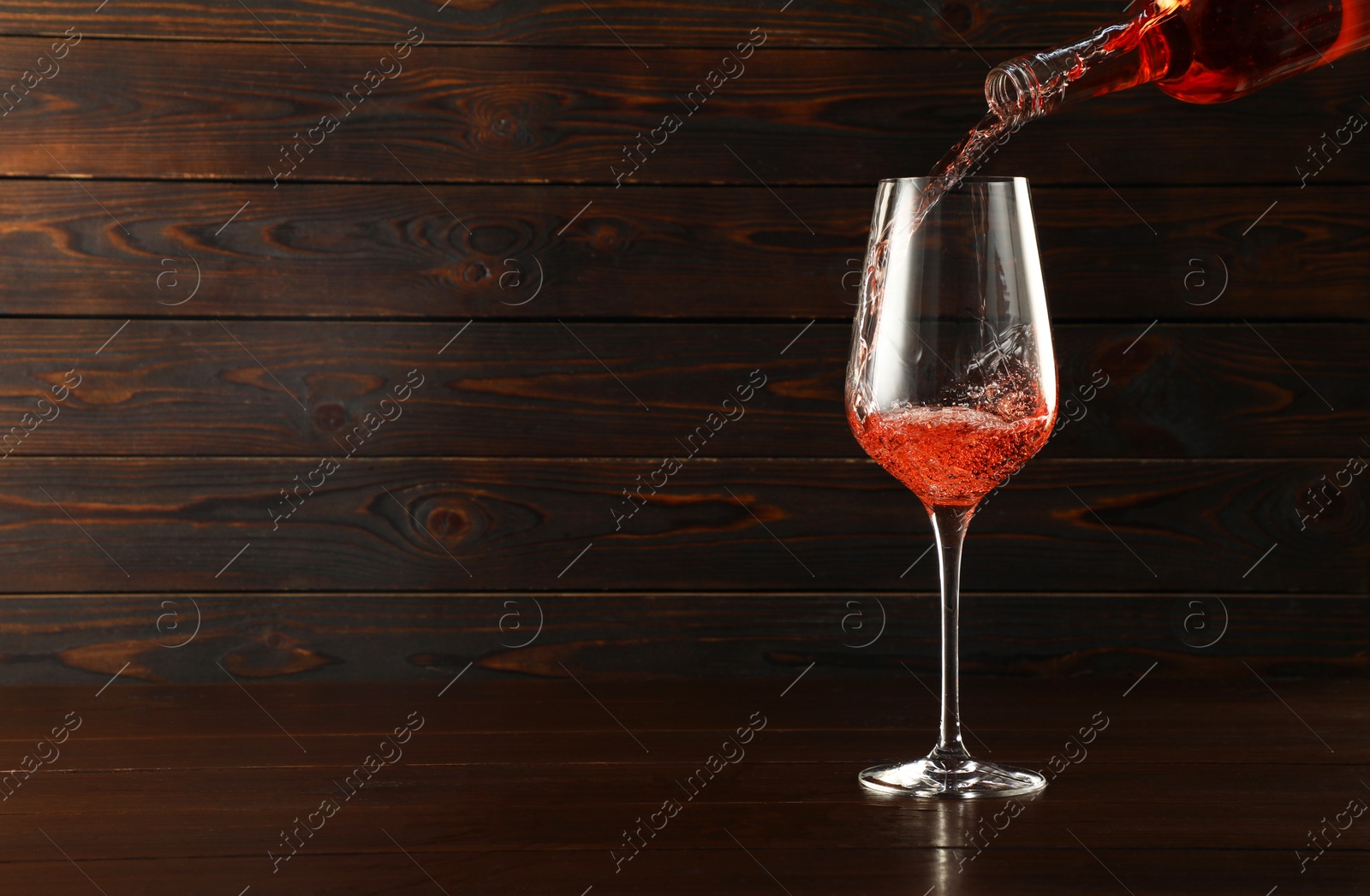 Photo of Pouring rose wine into glass at wooden table, space for text