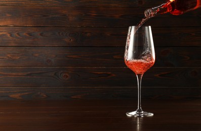 Photo of Pouring rose wine into glass at wooden table, space for text