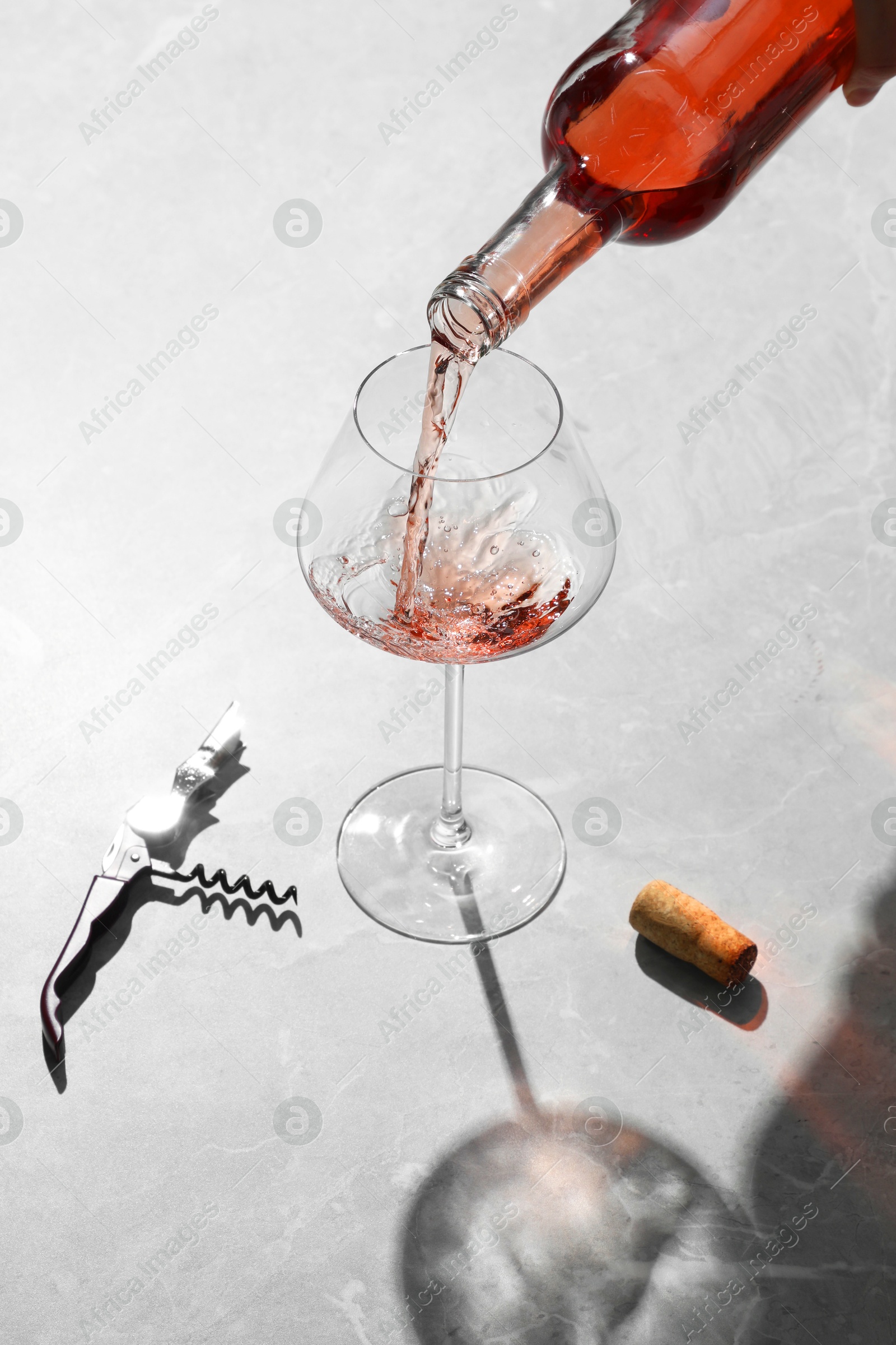 Photo of Pouring rose wine into glass at grey marble table