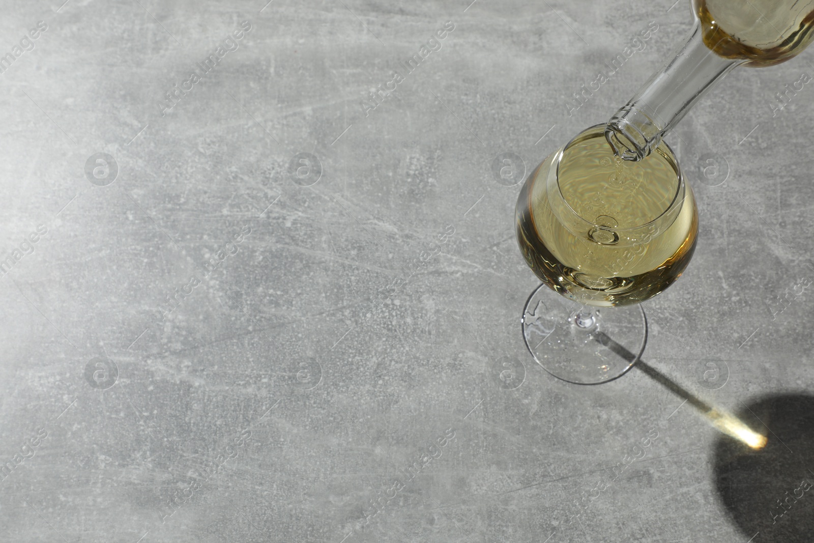 Photo of Pouring white wine into glass at grey table, above view. Space for text