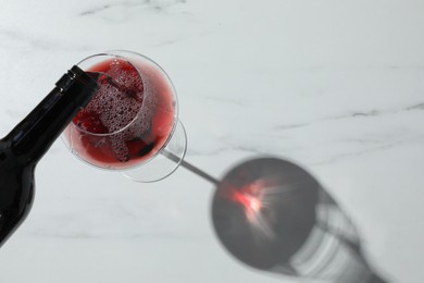 Photo of Pouring red wine into glass at white marble table, above view. Space for text