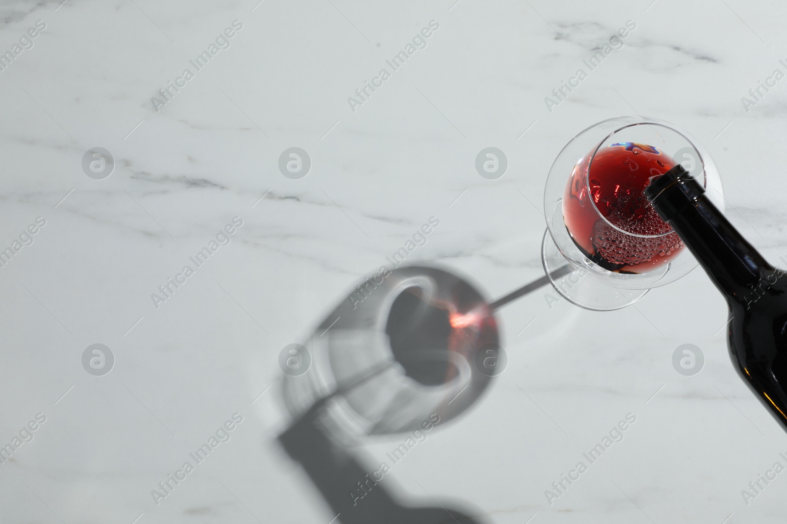 Photo of Pouring red wine into glass at white marble table, above view. Space for text