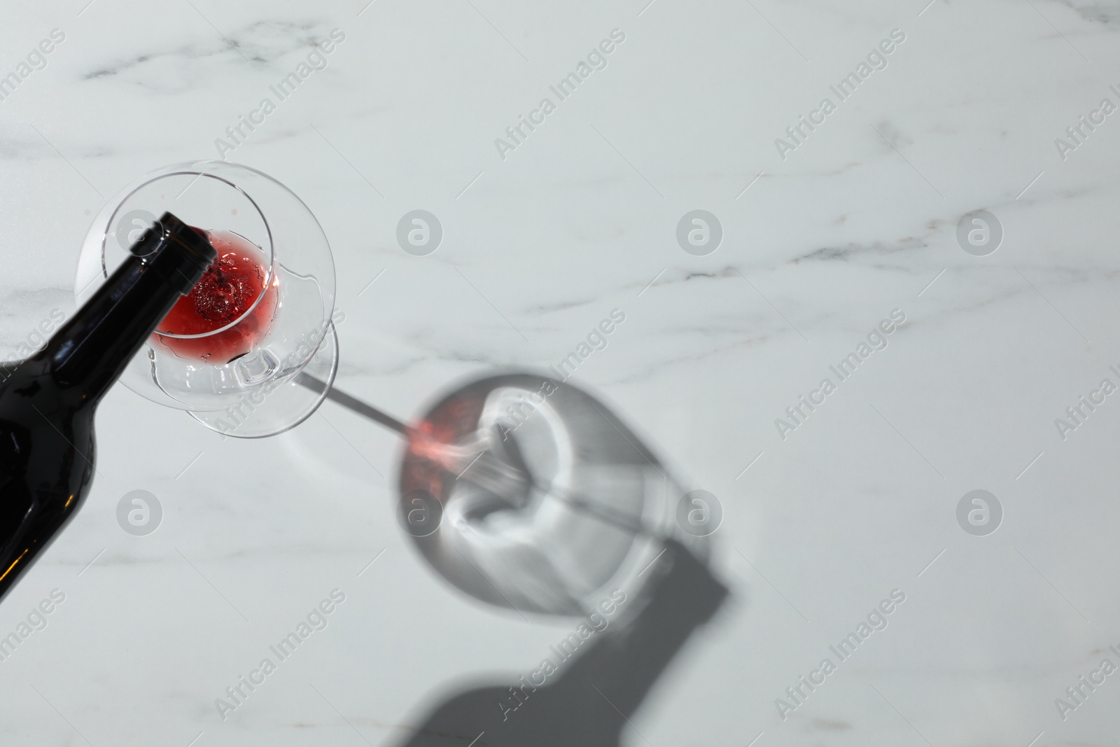 Photo of Pouring red wine into glass at white marble table, top view. Space for text