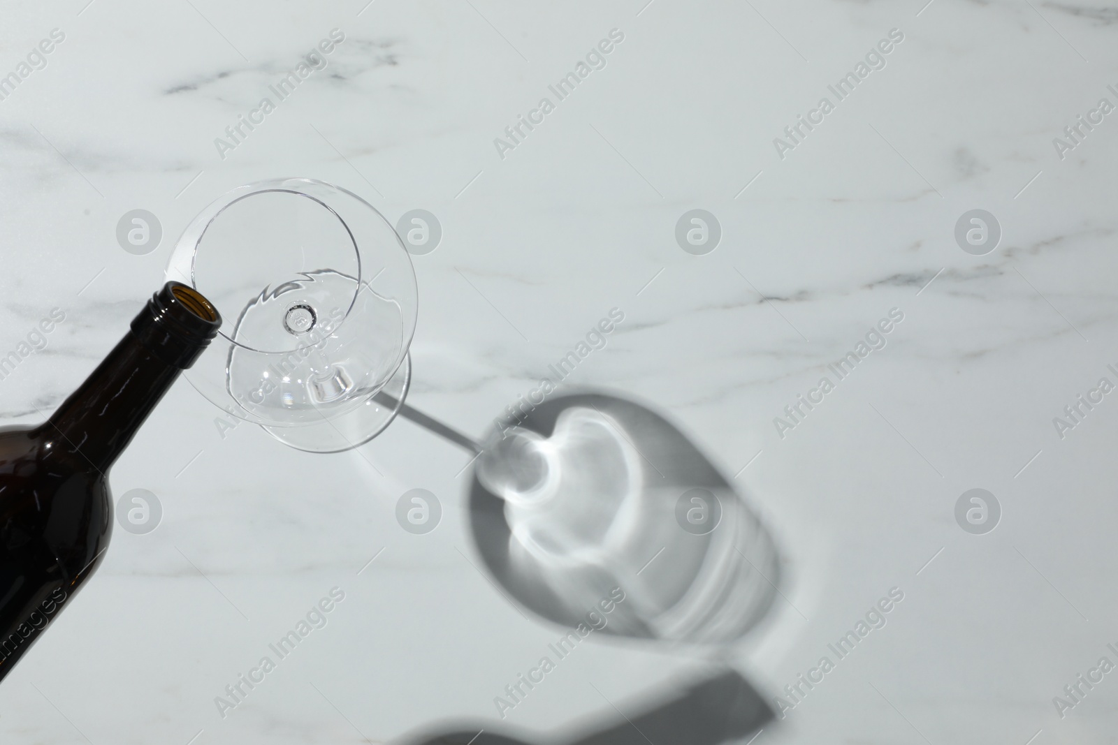 Photo of Pouring wine into glass at white marble table, top view. Space for text