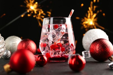 Photo of Tasty Christmas cocktail in glass and decor on black table against blurred lights, closeup