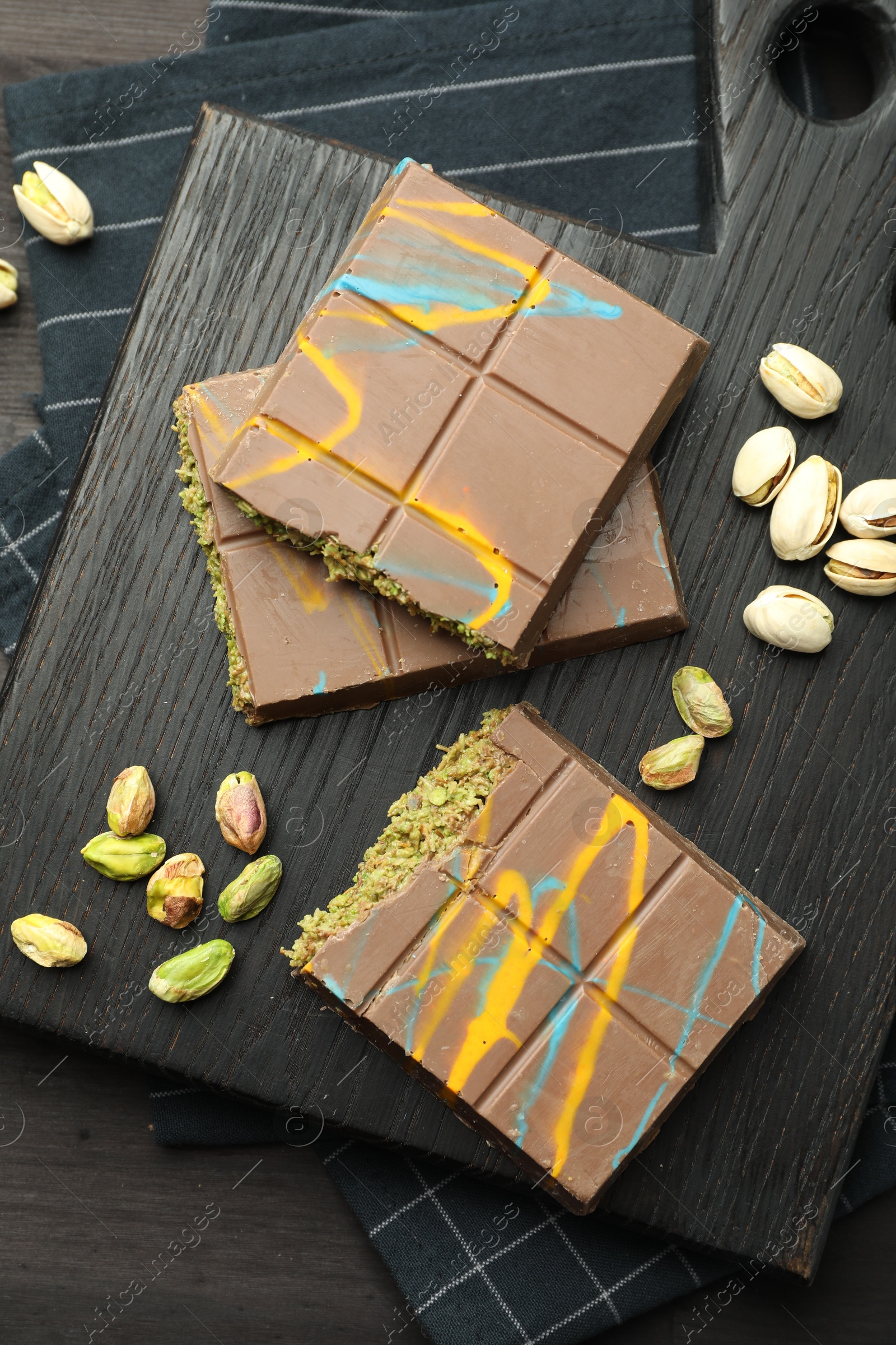 Photo of Pieces of Dubai chocolate bars with pistachios and knafeh on black wooden table, top view