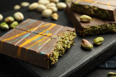 Photo of Pieces of Dubai chocolate bars with pistachios and knafeh on black table, closeup