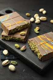 Photo of Pieces of Dubai chocolate bars with pistachios and knafeh on black wooden table, closeup