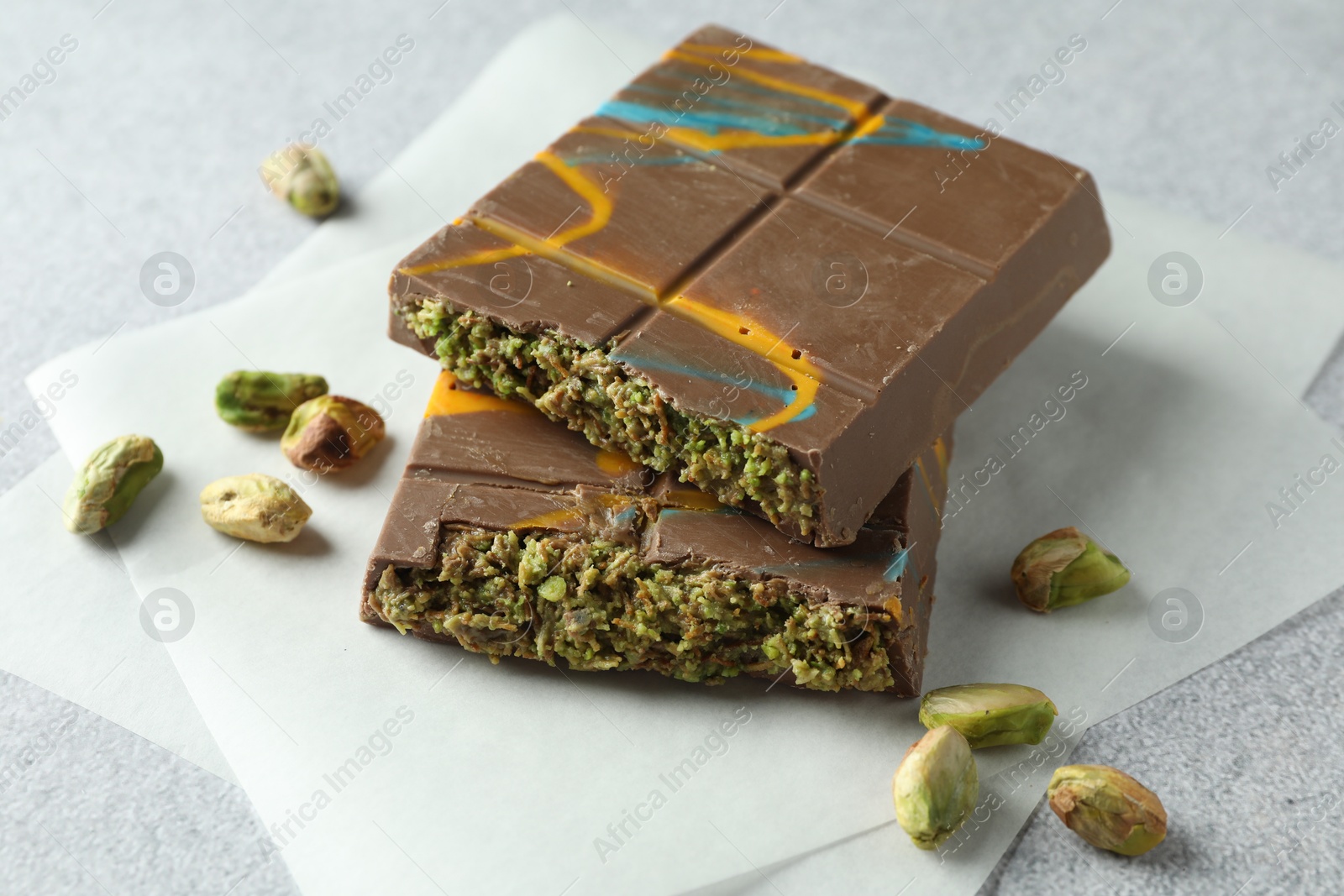 Photo of Pieces of Dubai chocolate bar with pistachios and knafeh on light grey table, closeup