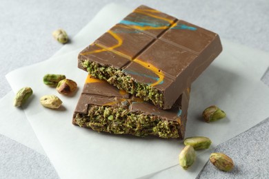 Photo of Pieces of Dubai chocolate bar with pistachios and knafeh on light grey table, closeup