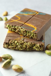 Photo of Pieces of Dubai chocolate bar with pistachios and knafeh on light grey table, closeup