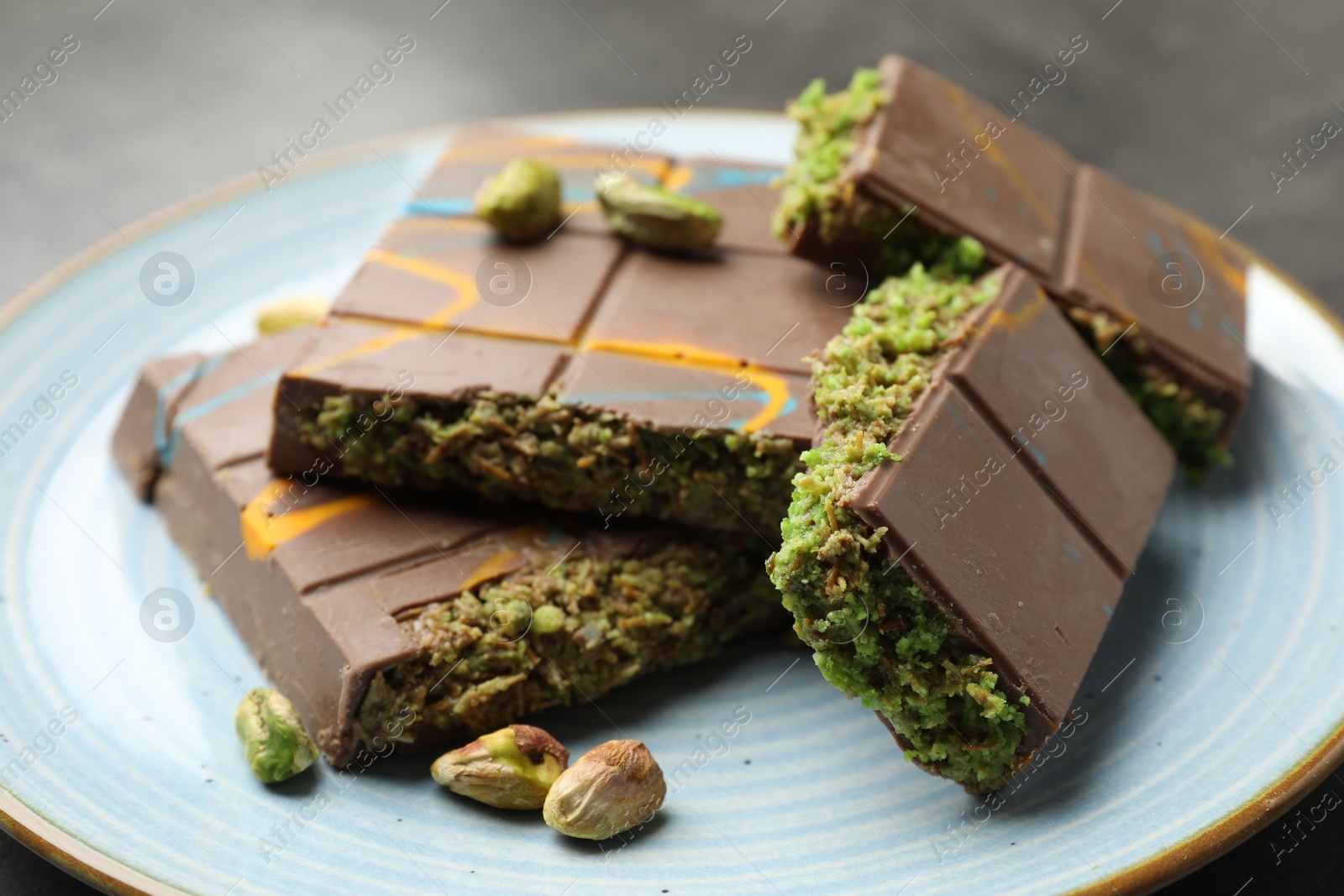 Photo of Pieces of Dubai chocolate bar with pistachios and knafeh on grey table, closeup