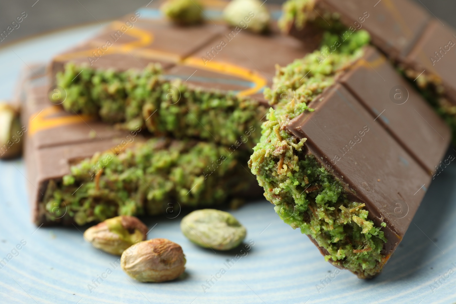 Photo of Pieces of Dubai chocolate bar with pistachios and knafeh on plate, closeup