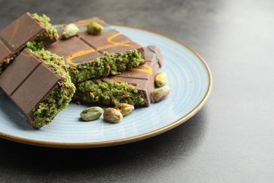 Photo of Pieces of Dubai chocolate bar with pistachios and knafeh on grey table, closeup. Space for text