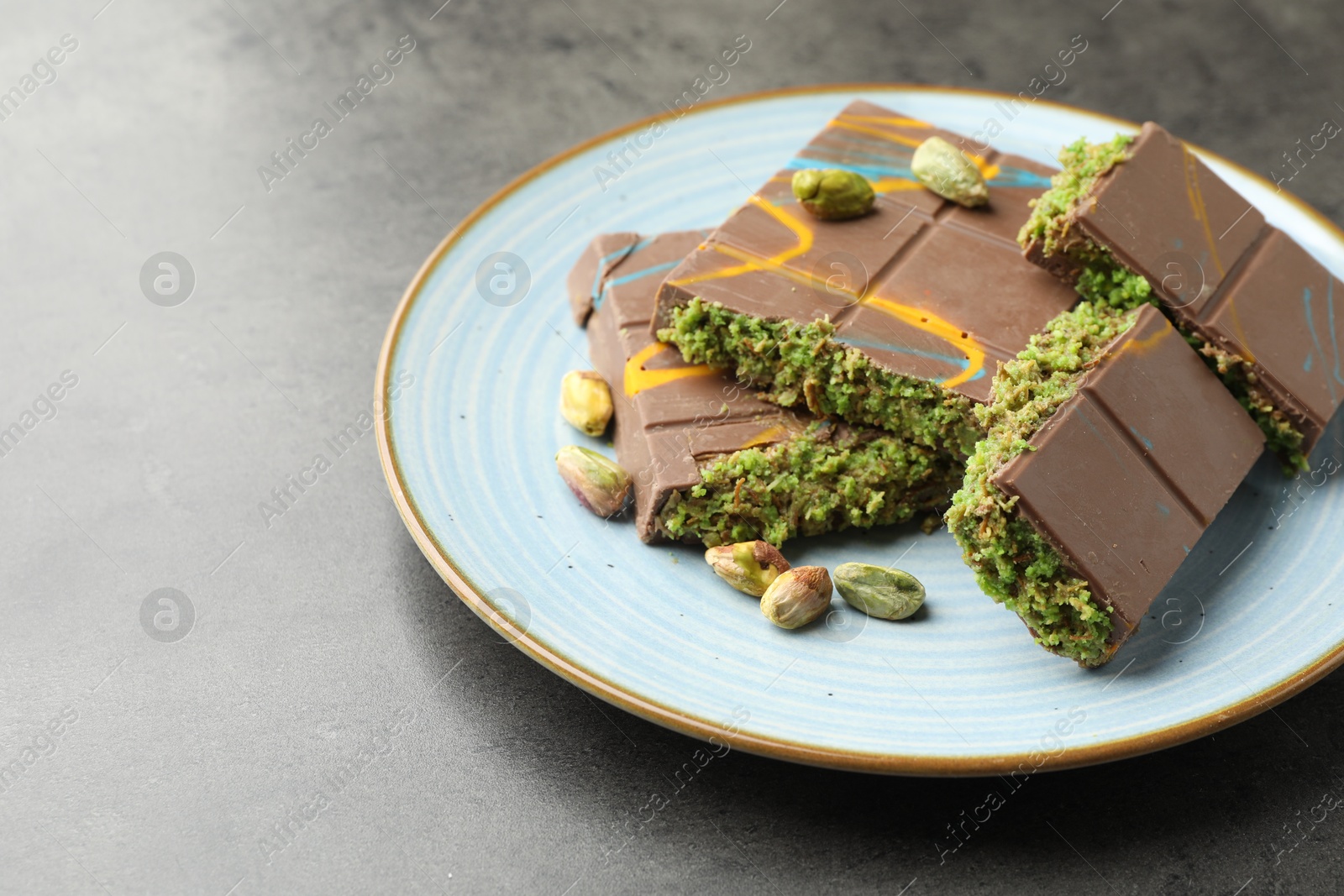 Photo of Pieces of Dubai chocolate bar with pistachios and knafeh on grey table, closeup. Space for text