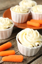 Photo of Delicious carrot muffins and fresh vegetables on wooden table, closeup