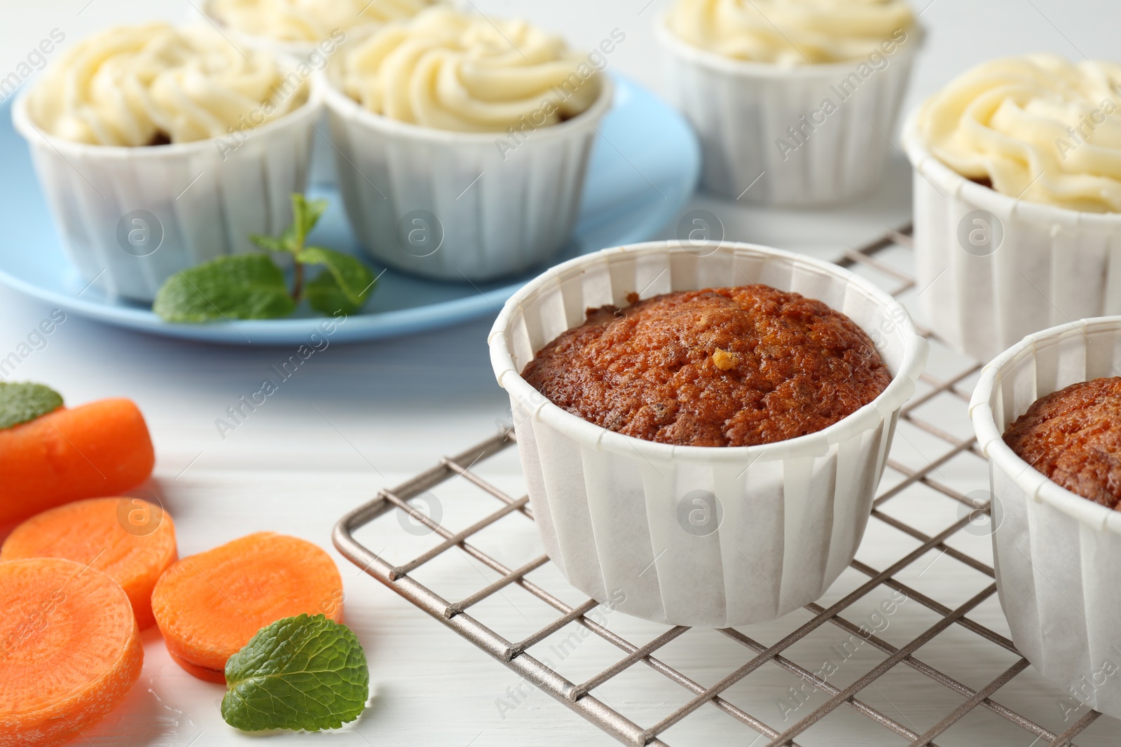 Photo of Delicious carrot muffins and fresh vegetable on white wooden table, closeup