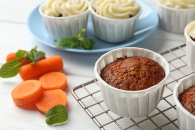 Photo of Delicious carrot muffins and fresh vegetable on white wooden table, closeup