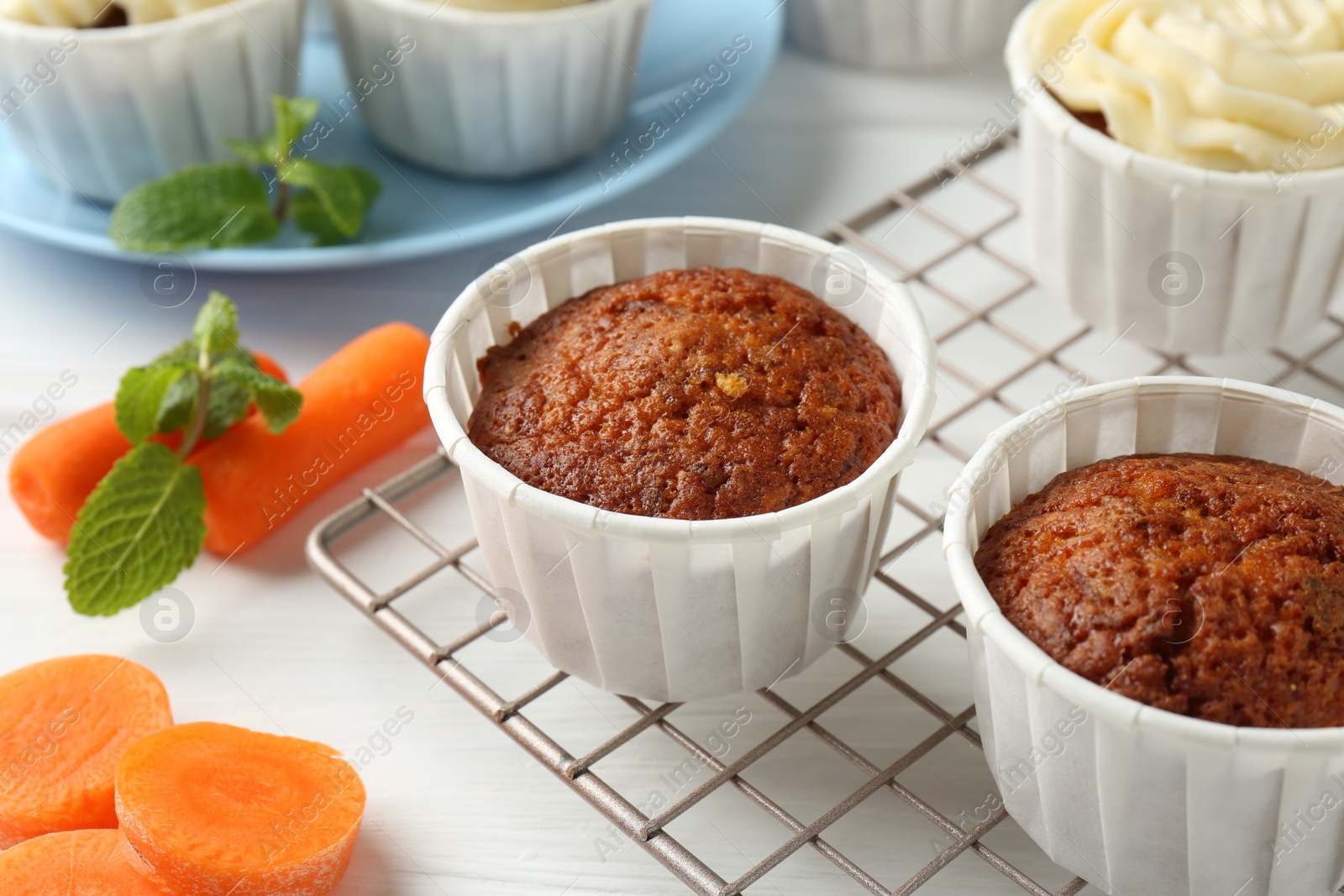 Photo of Delicious carrot muffins and fresh vegetables on white wooden table, closeup